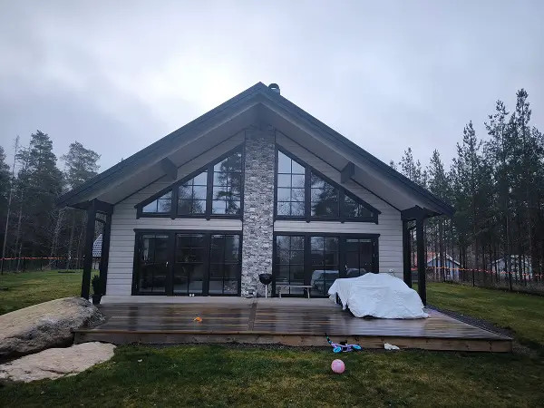 Modern villa med stora energieffektiva fönster efter fönsterbyte i Eskilstuna, vit fasad, glaspartier och träaltan omgivet av skog.